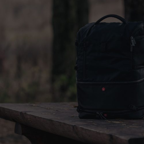 A black backpack sits on a wooden bench in the woods.