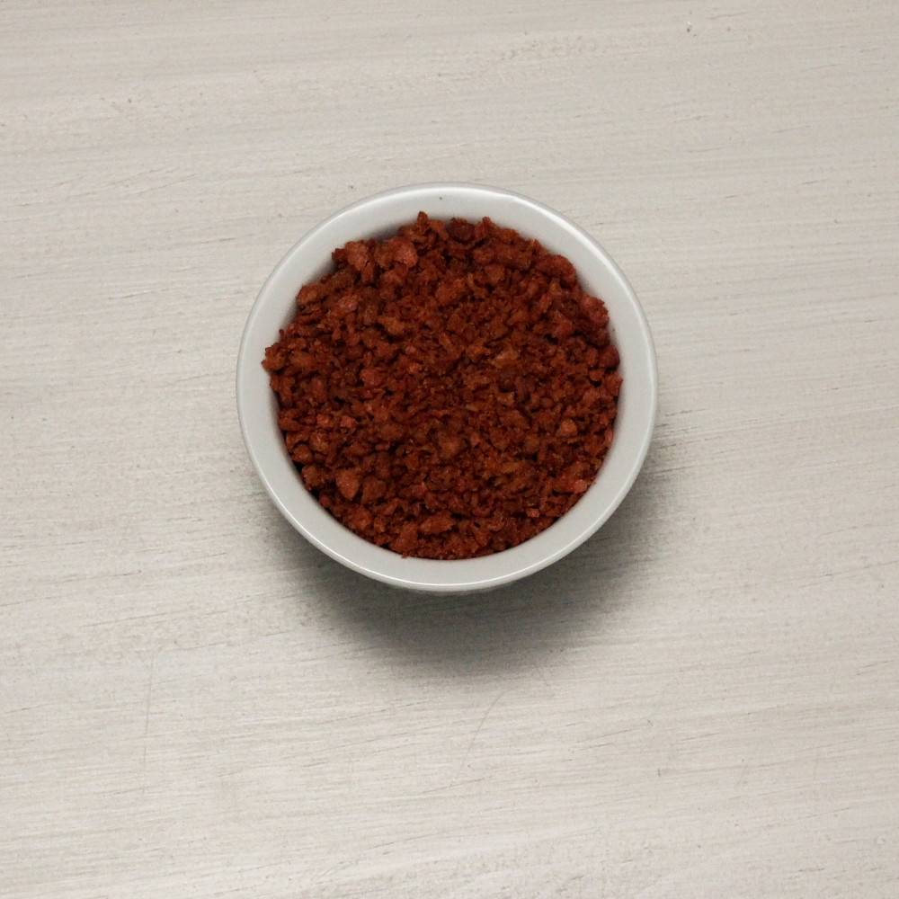 A small bowl of Augason Farms Bacon Flavored Bits Vegetarian Meat Substitute TVP 192 Servings #10 Can - (SHIPS IN 1-2 WEEKS) on a table.