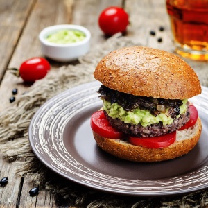 A gluten-free burger with guacamole and tomatoes on a plate.