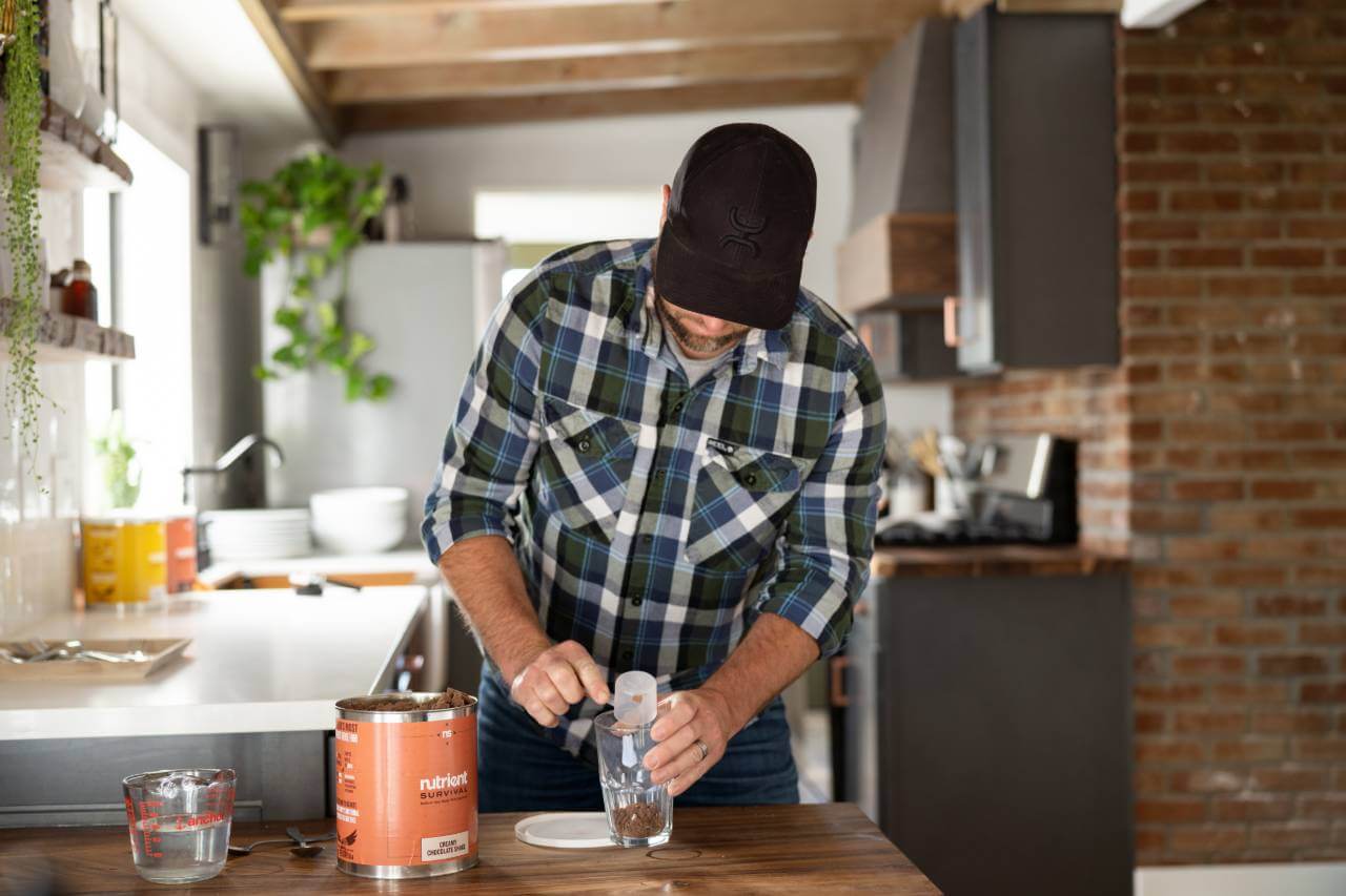 A man in a plaid shirt is painting a kitchen with Nutrient Survival Non-GMO Vegetarian Gluten-Free Creamy Chocolate Shake 15 Servings - (SHIPS IN 2-4 WEEKS).