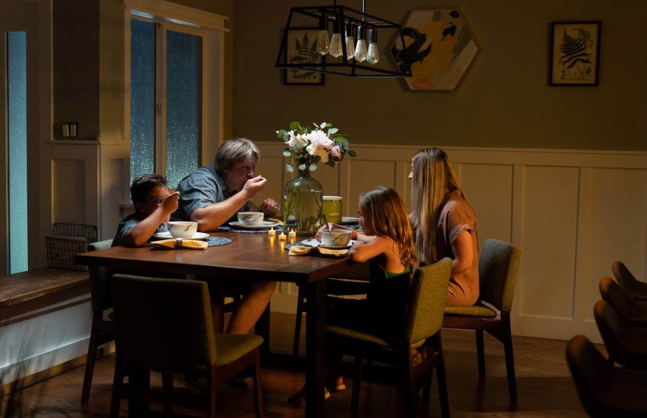 A family eats dinner at a table in a dark room, enjoying their Nutrient Survival Triple Cheese Mac 10 Servings - (SHIPS IN 2-4 WEEKS).