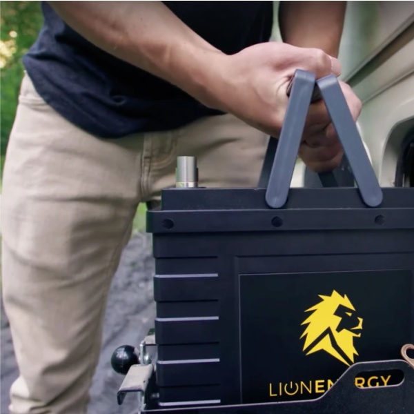 A man is holding a Lion Energy Lion Safari UT 1300 Deep Cycle Battery with a yellow label on it.