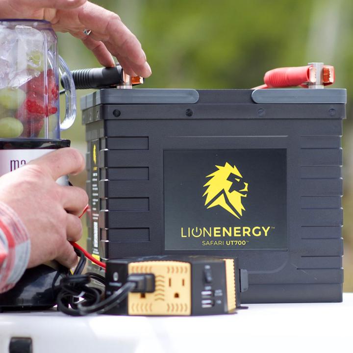 A man is putting a Lion Energy Lion Safari UT 700 Deep Cycle Battery on a table.