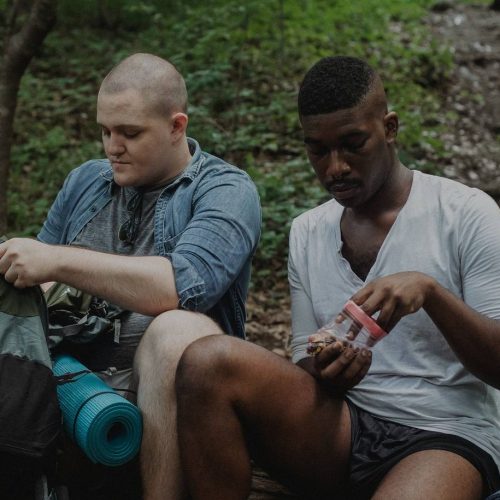 Two men sitting in the woods with backpacks.