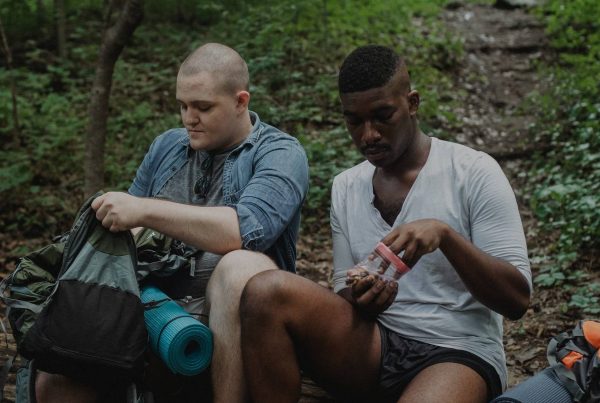 Two men sitting in the woods with backpacks.