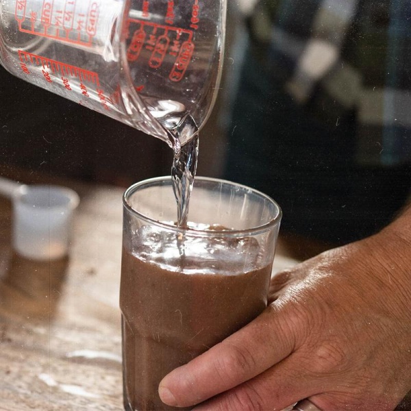 A person pouring Nutrient Survival Non-GMO Vegetarian Gluten-Free Creamy Chocolate Shake SINGLES - (SHIPS IN 2-4 WEEKS) into a glass.