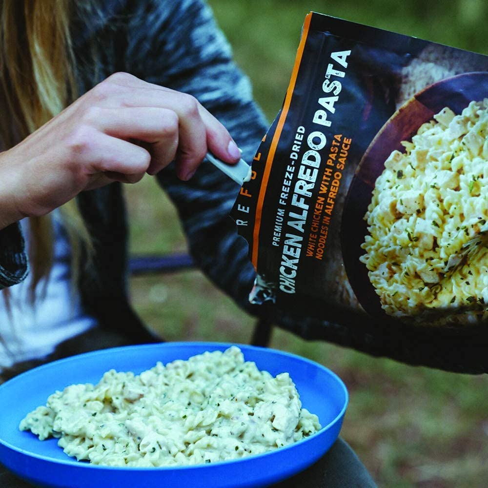 A woman eating a Peak Refuel Traverse Pack Variety Meals Food Storage and Backpacking Food Kit (SHIPS IN 1-2 WEEKS) in the woods.