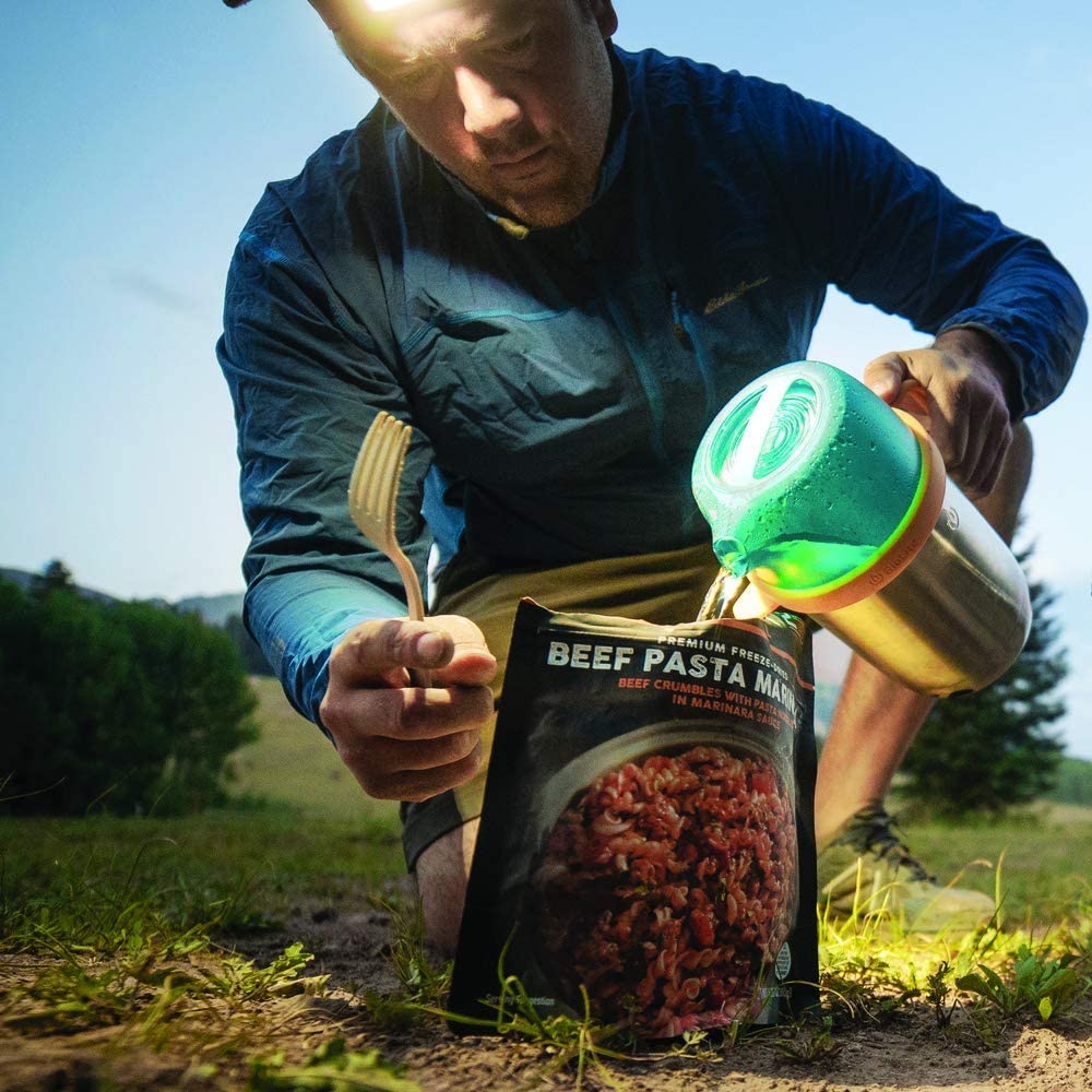 A man pouring Peak Refuel Freeze-Dried Entree Variety Pack Food Storage and Backpacking Food Kit - (SHIPS IN 1-2 WEEKS) into a bag on the ground.
