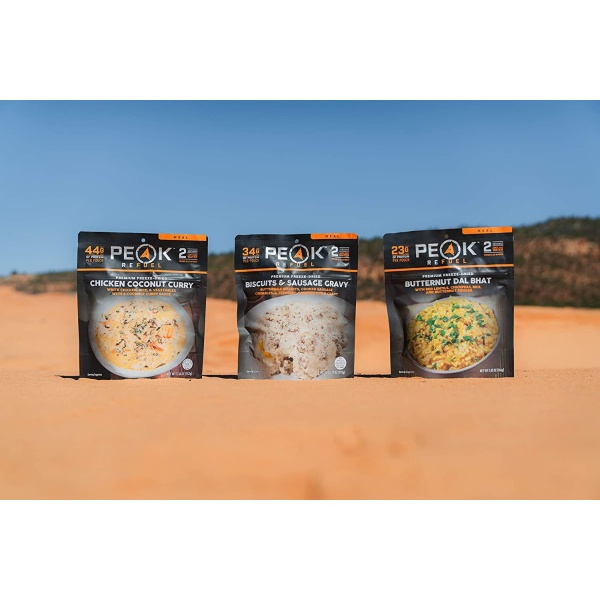 Three packages of Peak Refuel Freeze-Dried Breakfast, Lunch, and Dinner Sampler Food Storage and Backpacking Food Kit - (SHIPS IN 1-2 WEEKS) sitting on top of a sand dune.