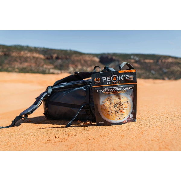 A backpack with a Peak Refuel Freeze-Dried Breakfast, Lunch, and Dinner Sampler Food Storage and Backpacking Food Kit - (SHIPS IN 1-2 WEEKS) sitting on top of a sand dune.