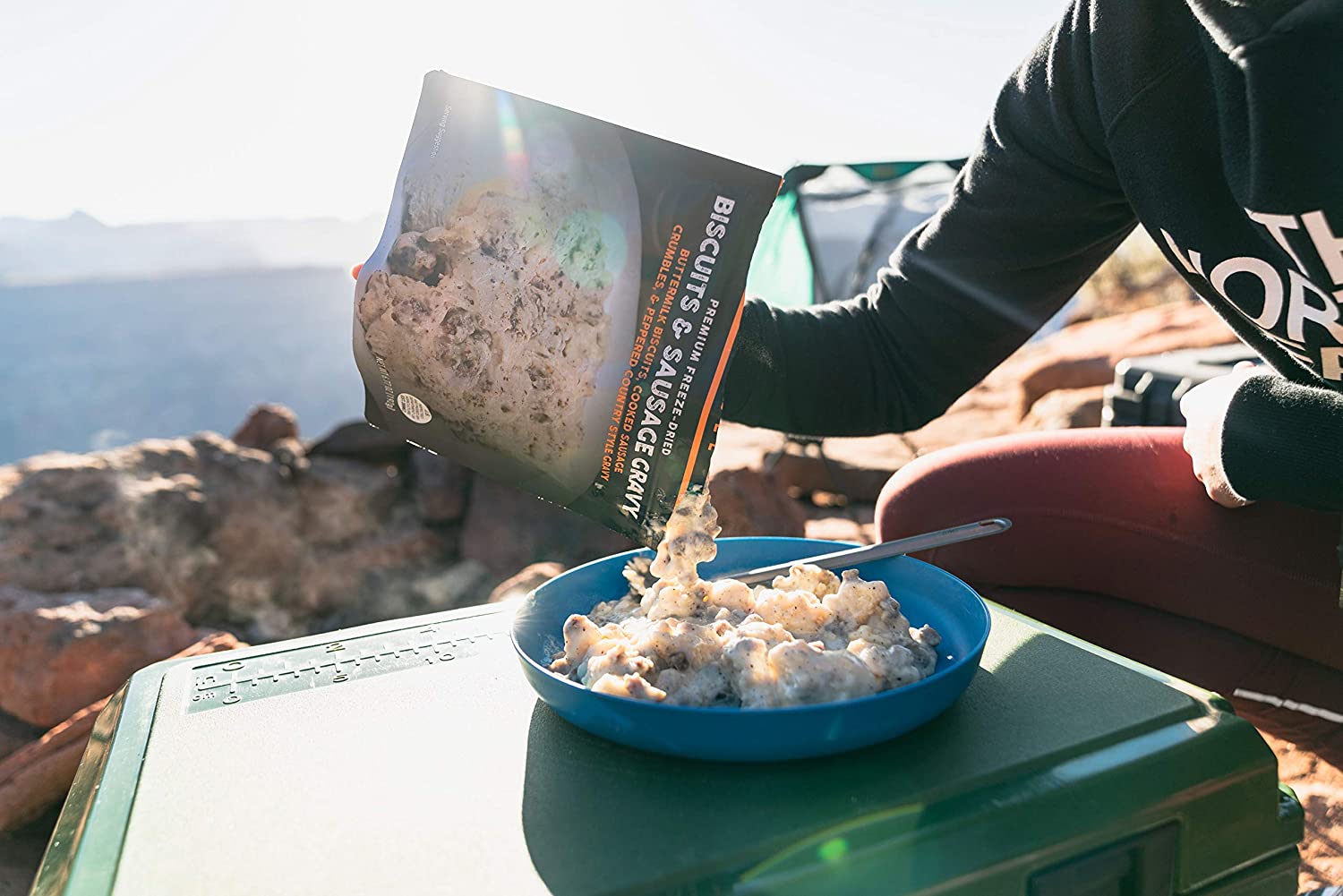 A person eating a Peak Refuel Freeze-Dried Breakfast Sampler Food Storage and Backpacking Food Kit - (SHIPS IN 1-2 WEEKS) on top of a mountain.