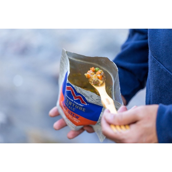 A person holding a Mountain House Beef Stew Pouch - Gluten-Free - 2 Servings - (SHIPS IN 1-2 WEEKS) with a wooden spoon.