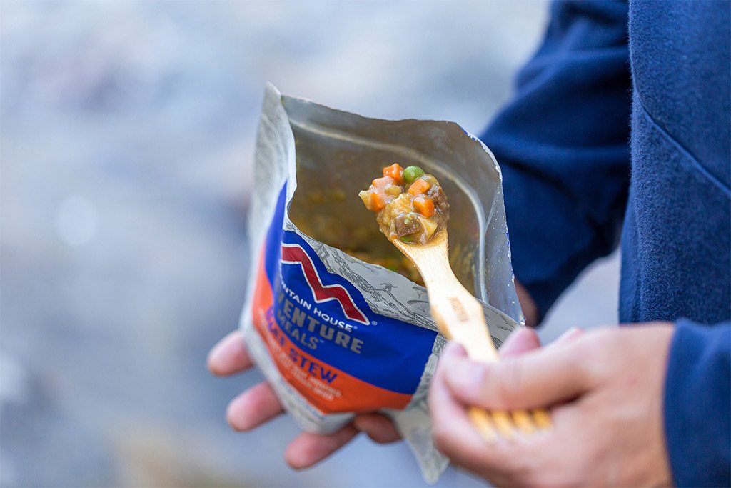 A person holding a Mountain House Beef Stew Pouch - Gluten-Free - 2 Servings - (SHIPS IN 1-2 WEEKS) with a wooden spoon.
