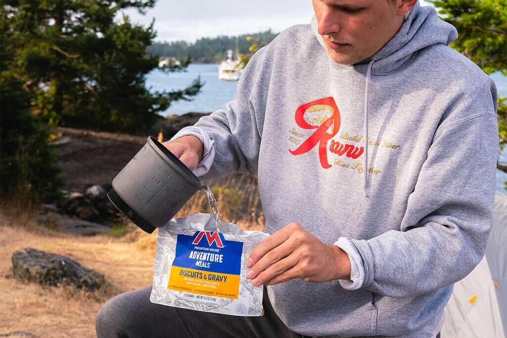 A man in a hoodie holding a Mountain House Biscuits and Gravy Mylar Pouch - 2 Servings - (SHIPS IN 1-2 WEEKS).