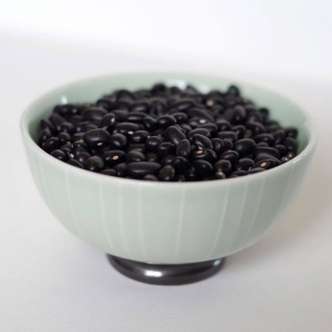 Black beans in a bowl on a white surface.