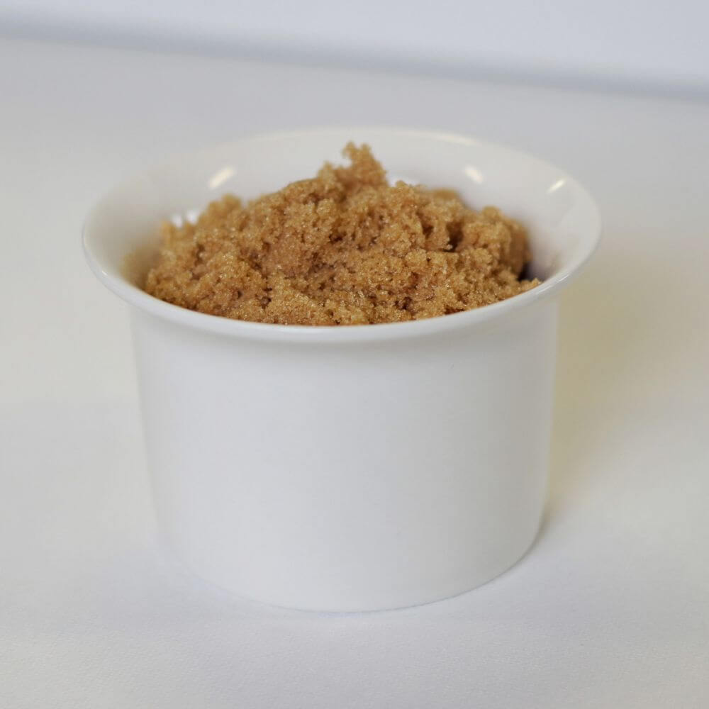 A white bowl with brown sugar in it.