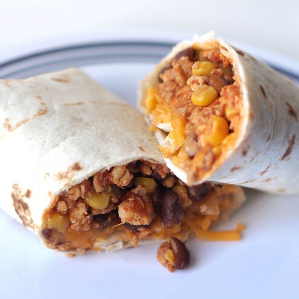 A burrito with meat, beans and corn on a plate.