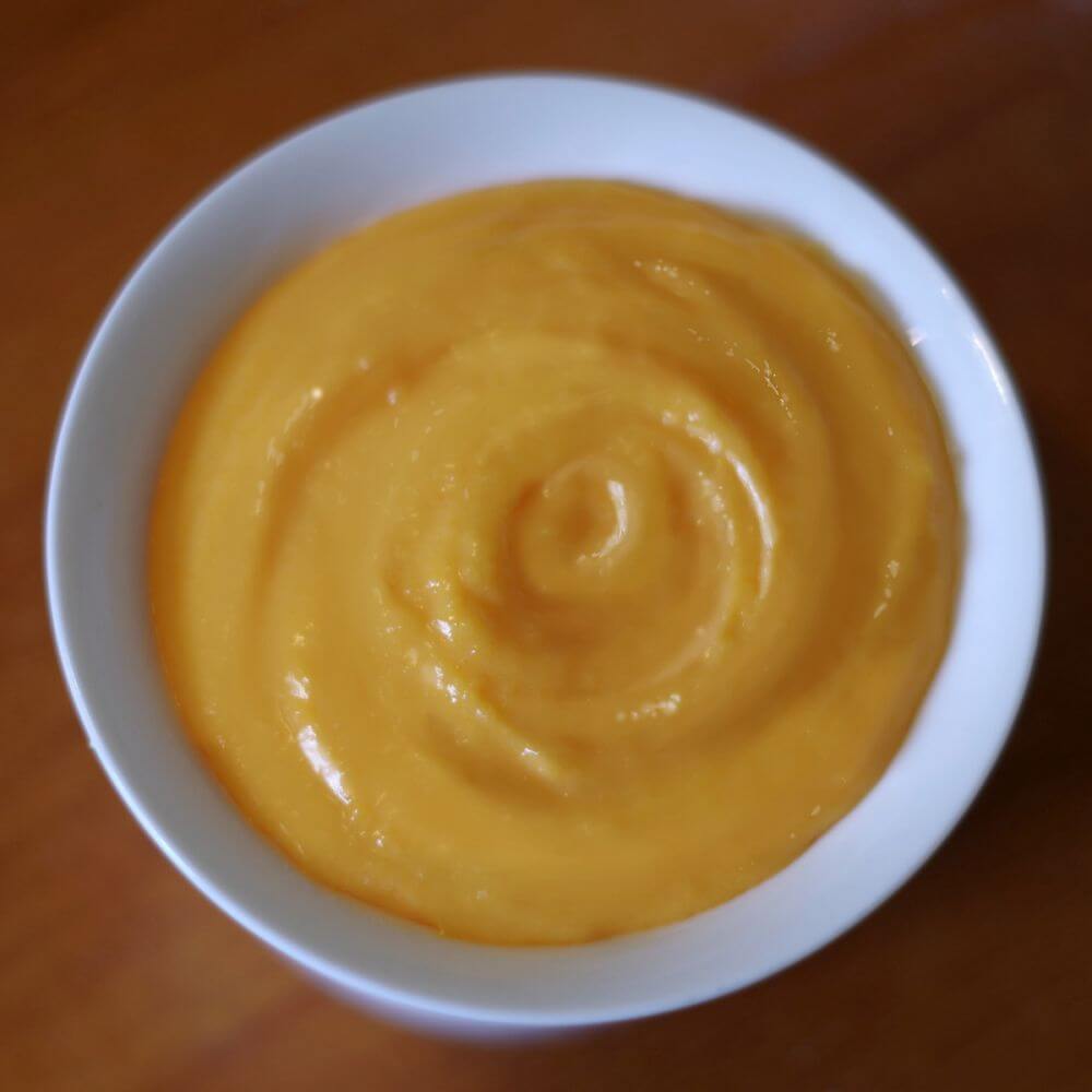 A bowl of orange sauce on top of a wooden table.