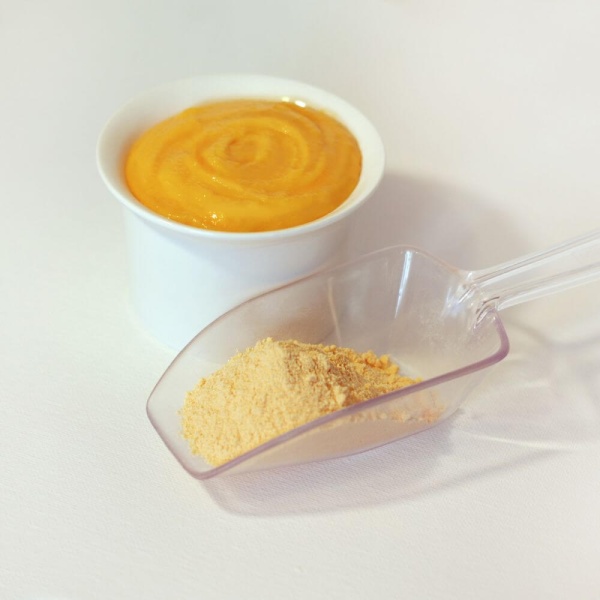 A scoop of powder next to a bowl of orange juice.