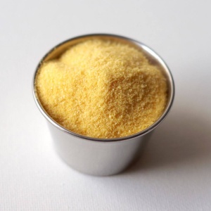 A cup of yellow sugar sitting on a white surface.