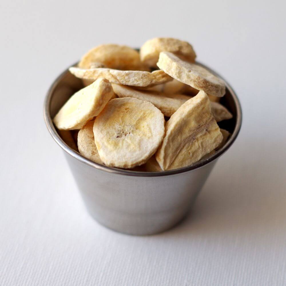 Banana chips in a metal bowl on a white surface.