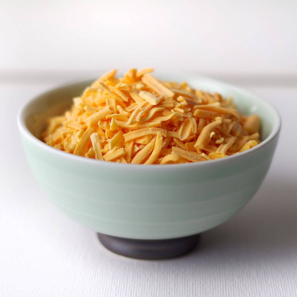 Shredded cheese in a bowl on a white surface.