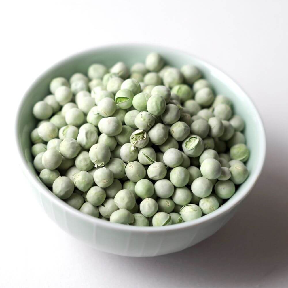 Peas in a bowl on a white surface.