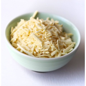 Shredded cheese in a bowl on a white surface.