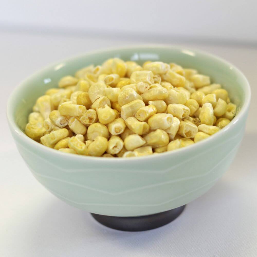 Corn in a bowl on a white surface.