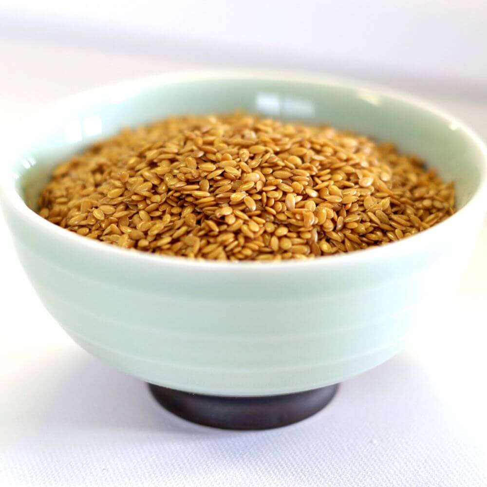 Fenugreek seeds in a bowl on a white surface.