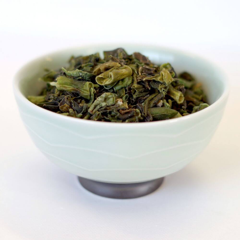 Green tea in a bowl on a white surface.