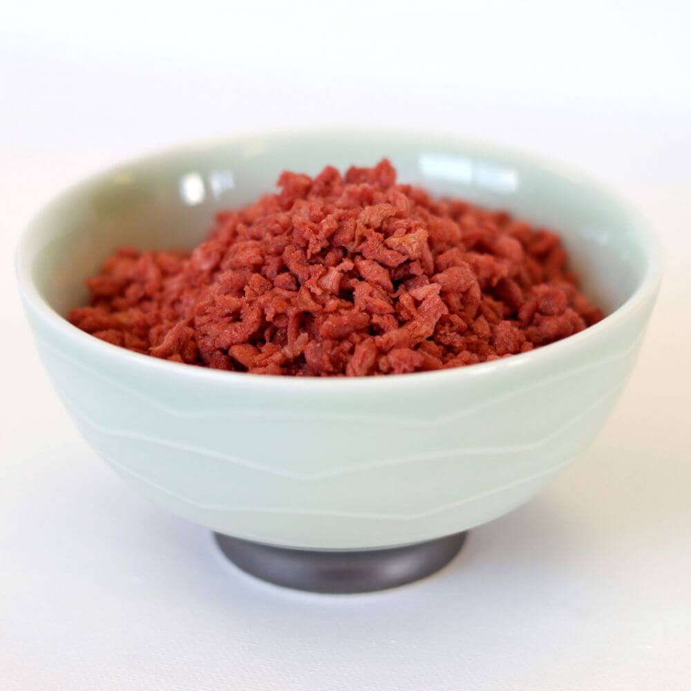 Red meat in a bowl on a white surface.