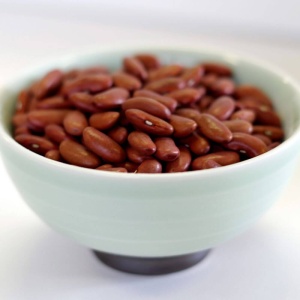 Red kidney beans in a bowl on a white surface.