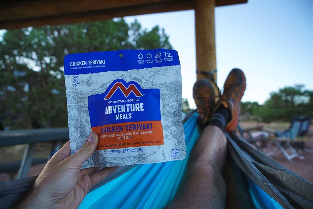 A person sitting in a hammock holding a Mountain House Chicken Teriyaki with Rice Mylar Pouch - 2 Servings - (SHIPS IN 1-2 WEEKS).