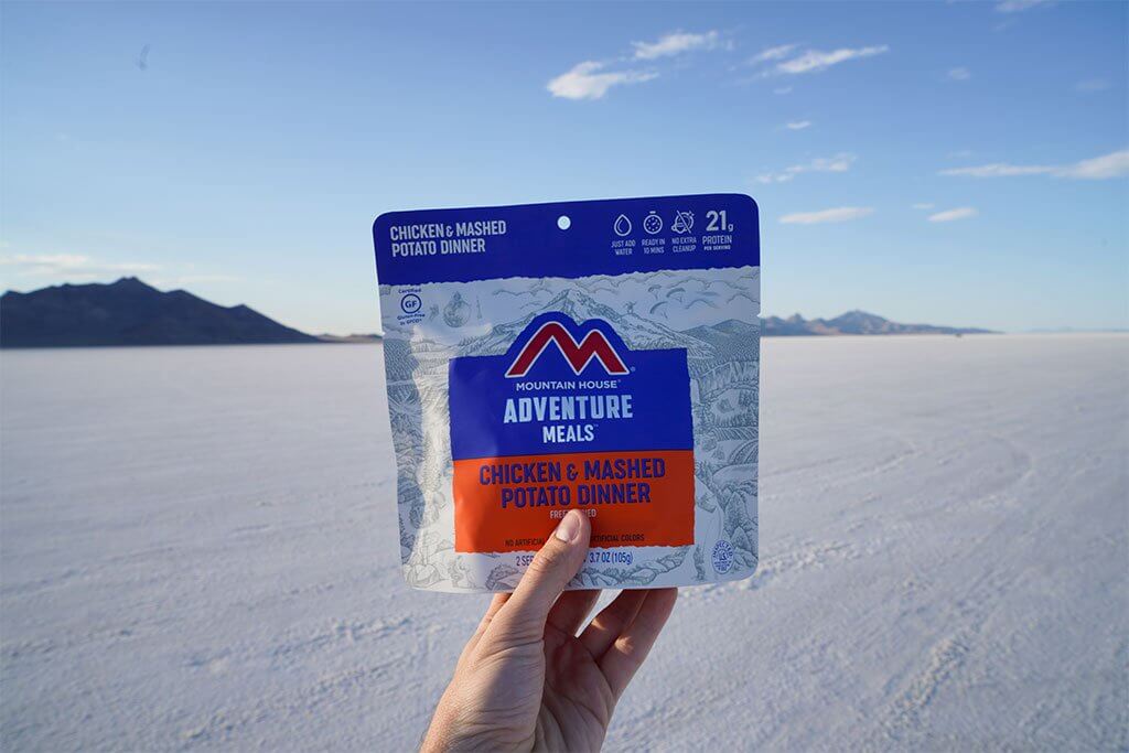 A person holding up a bag of Mountain House Chicken with Mashed Potatoes Mylar Pouch - Gluten-Free - 2 Servings - (SHIPS IN 1-2 WEEKS) salts.