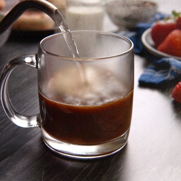 A mug with a cup of 100% Colombian Arabica coffee being poured into a glass.