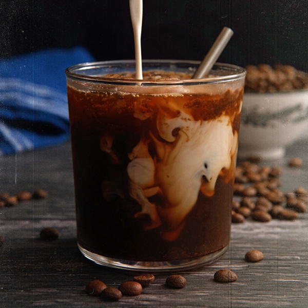 A glass of iced coffee with whipped cream and coffee beans made from 100% Colombian Arabica Coffee.