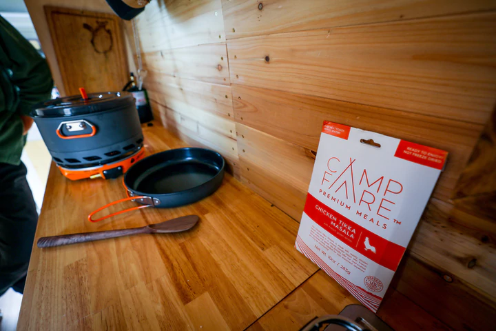 A man is cooking chicken tikka masala on a stove in a tiny house.