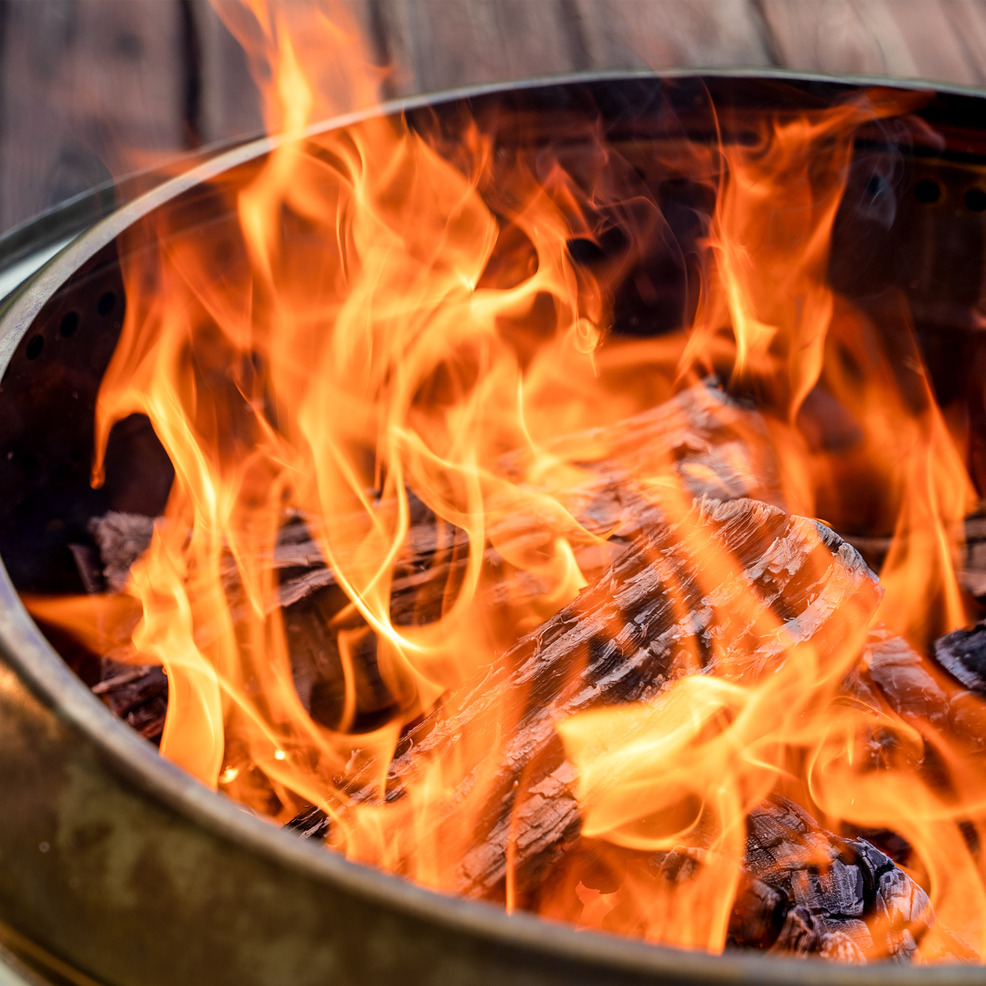 A portable fire pit with flames on a wooden deck.