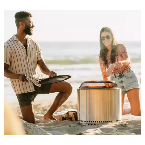 A man and woman enjoying a portable, "smokeless" fire pit on the beach.