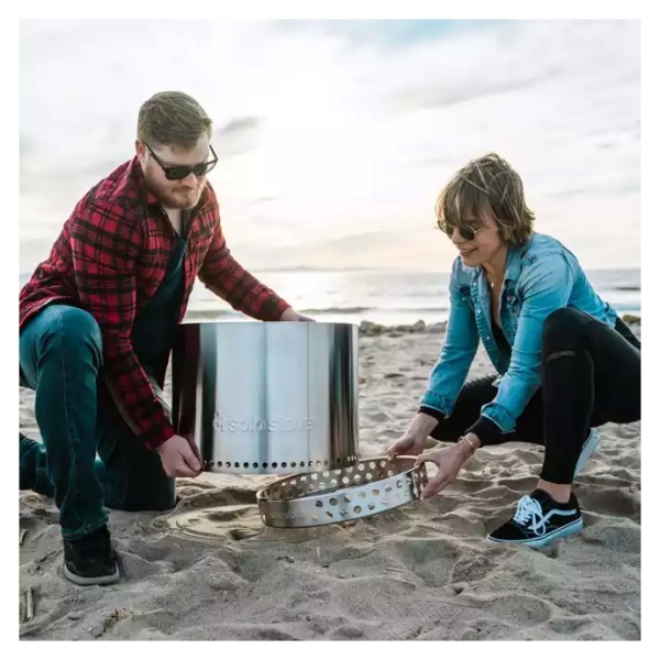 A couple setting up a portable fire pit on the beach.