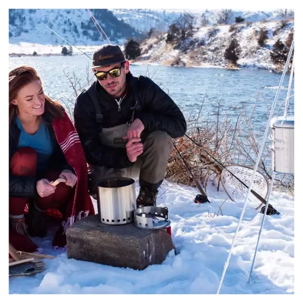 A couple sitting in the snow next to a Solo Stove campfire.