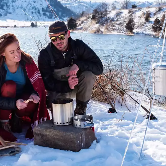 A couple sitting in the snow next to a Solo Stove campfire.