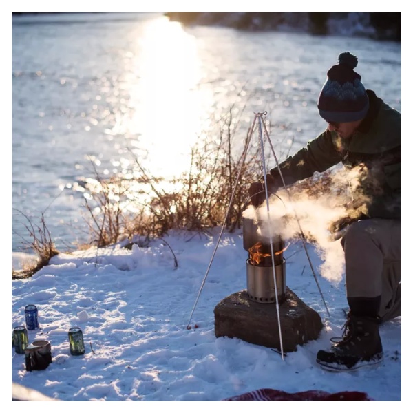 A man is cooking on a portable stove in the snow.