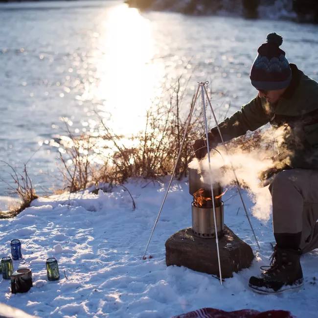 A man is cooking on a portable stove in the snow.