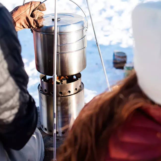 A woman is cooking food on a portable camp stove in the snow.
Keywords: Portable & "Smokeless