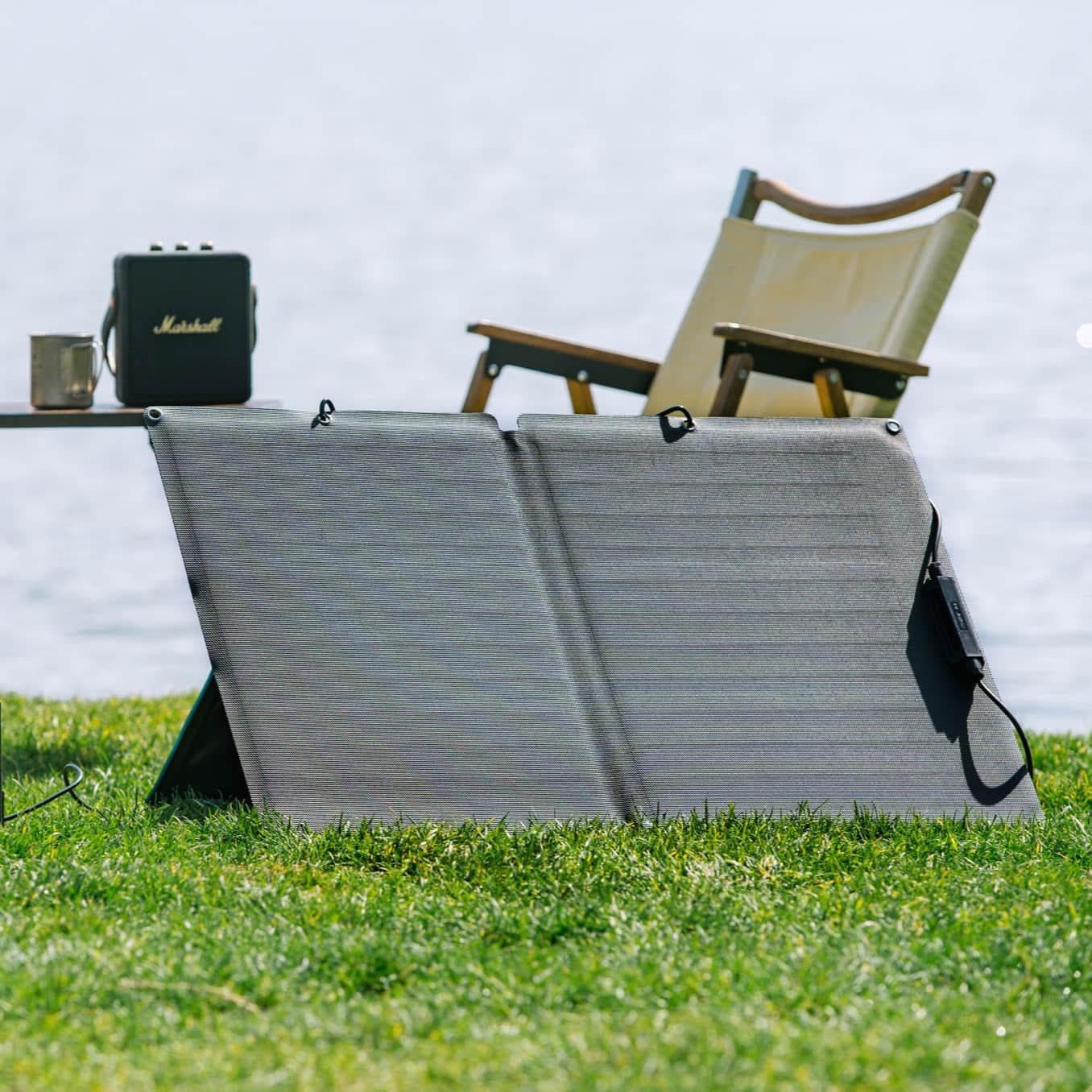 A portable solar panel sitting on the grass next to a lawn chair.