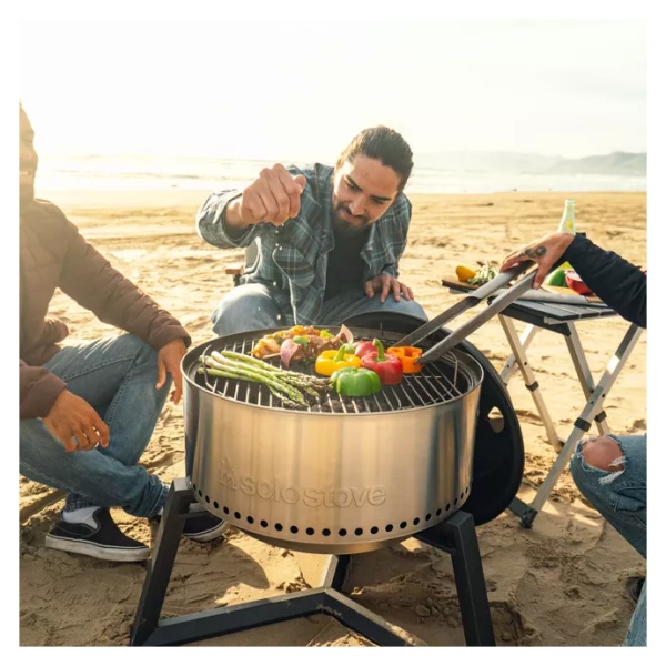 A group of people sitting around a portable grill on the beach.