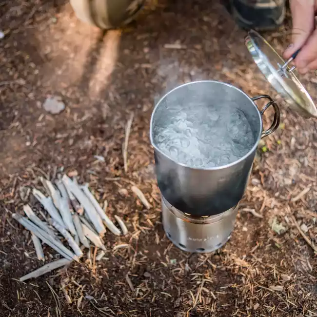 A person pouring water into a portable camp stove on the ground.