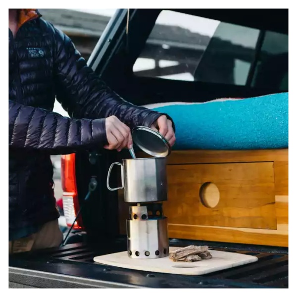 A man is making "coffee" in the back of a truck using a "portable" camp stove.